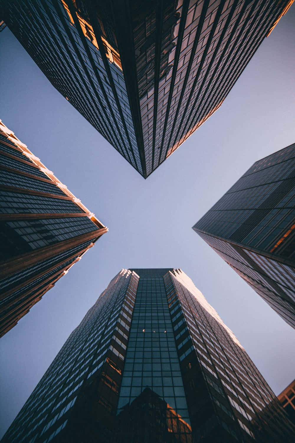  壁紙 — 高聳的玻璃摩天大樓在戲劇性的低角度城市拍攝中向清澈的藍天匯聚。