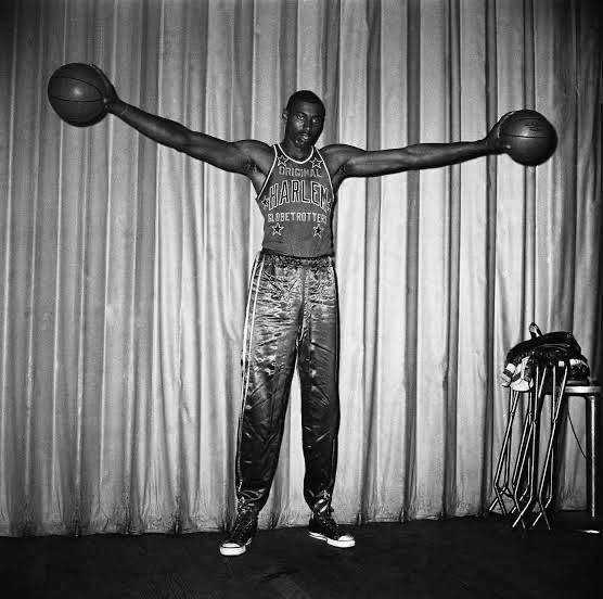 高大的哈林環球旅行者球員在舞台上伸展雙臂持籃球。 — NBA 壁紙