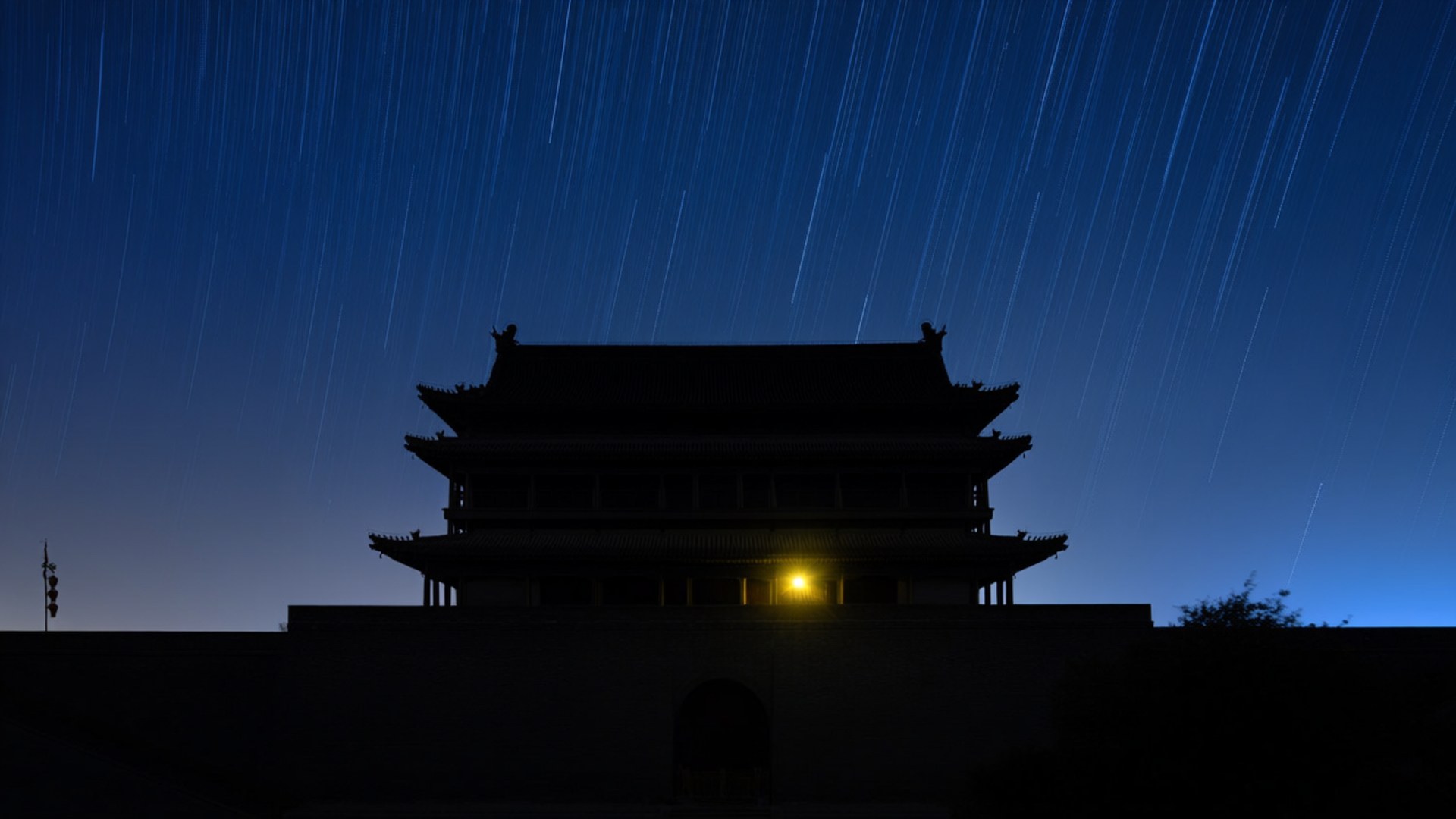 Starry Night Over Drum Tower 壁紙 — 傳統中國門樓的剪影矗立在深藍色天空下，天空中有明亮的星軌。