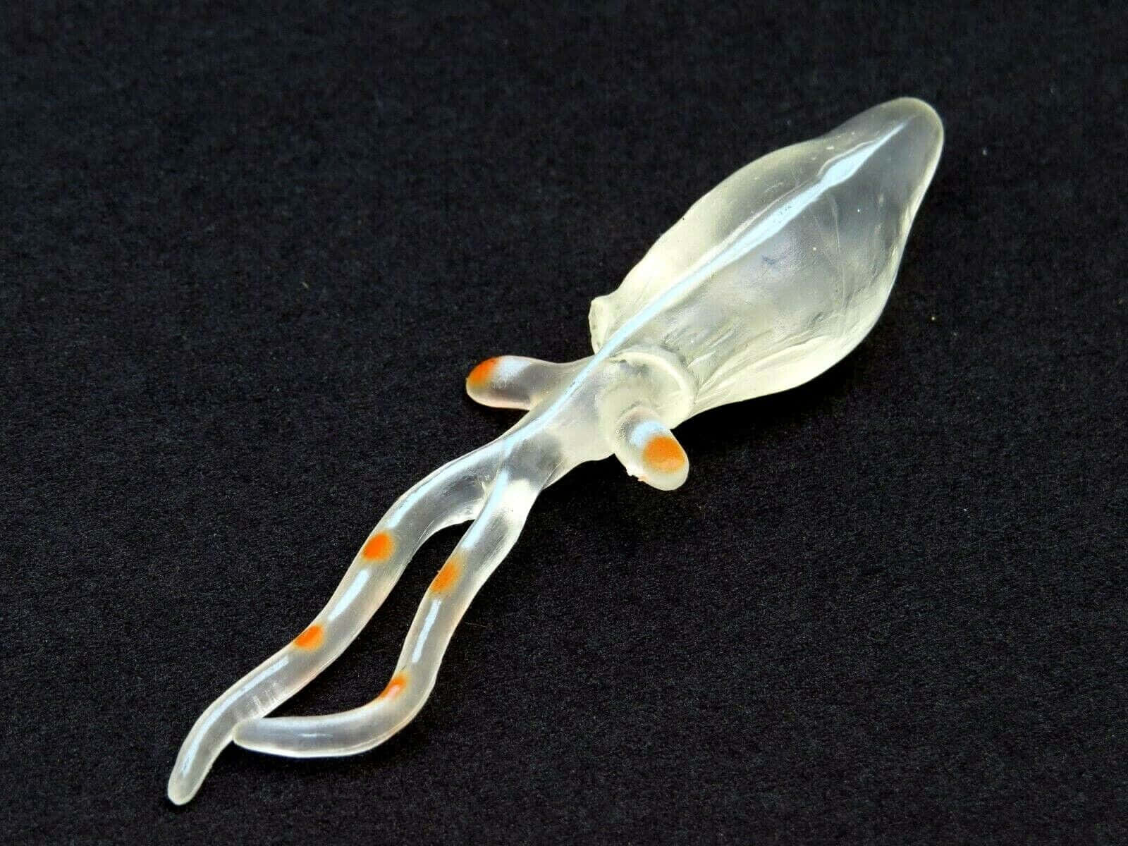  壁紙 — 一個半透明玻璃魷魚公仔，帶有橙色斑點，放置在深色紋理表面上。