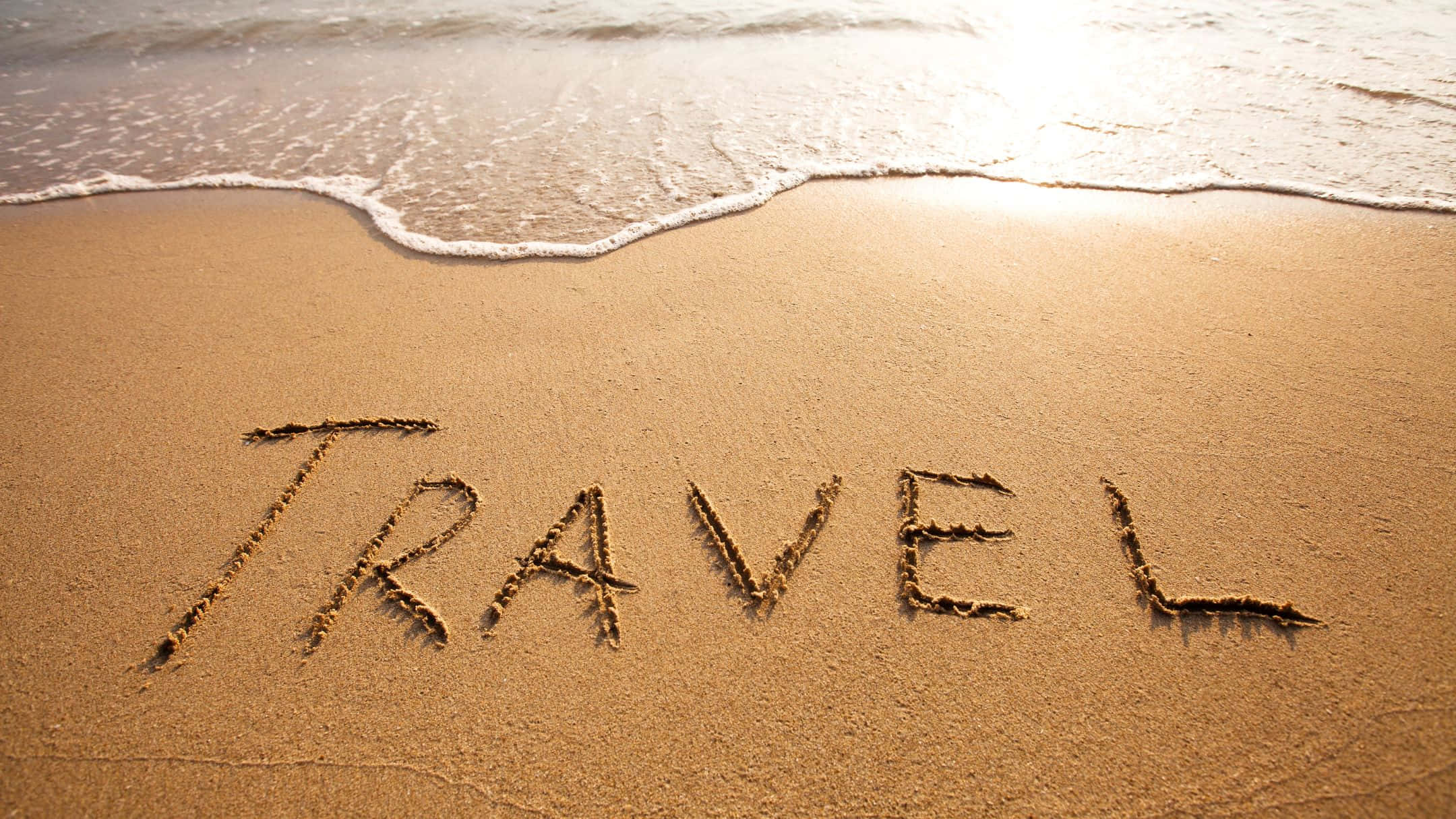 海灘 桌布 壁紙 — 「travel」這個字寫在沙灘上，溫柔的海浪在日落時分湧了過來。