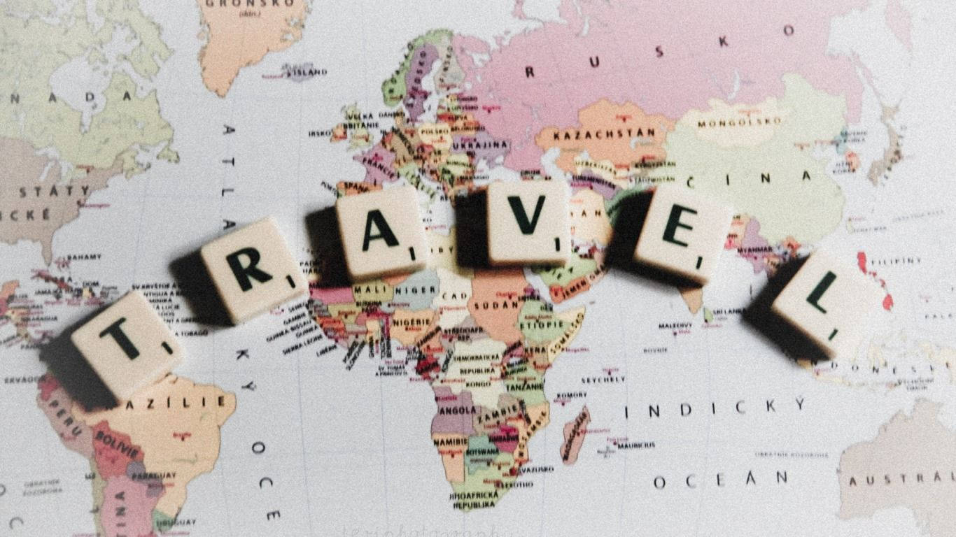 旅行 桌布 壁紙 — 「travel」這個字用木製字母拼砌，放在一張色彩繽紛的復古世界地圖上面。