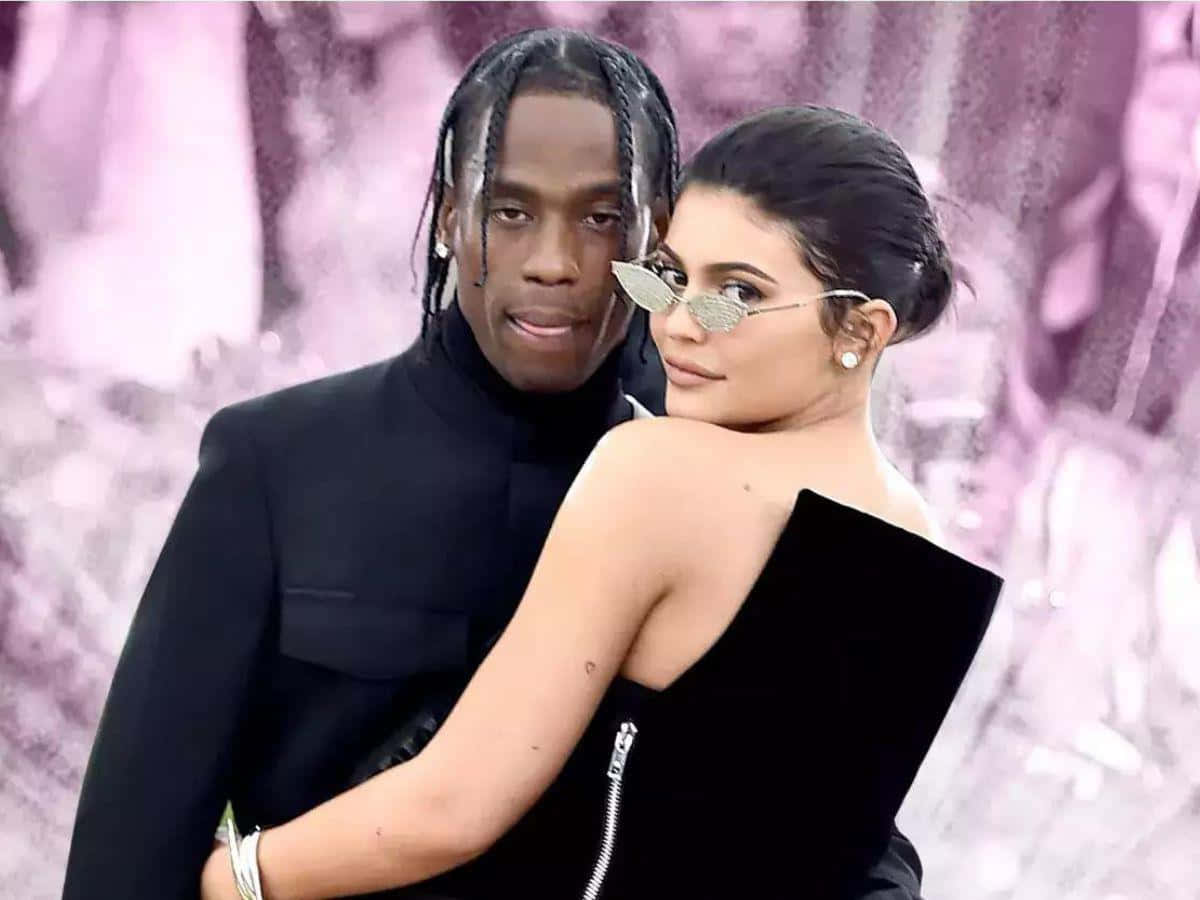 崔維斯·史考特 桌布 壁紙 — Travis Scott 和 Kylie Jenner 穿著黑色服裝在柔軟的粉紅色紋理背景前緊密地擺姿勢。