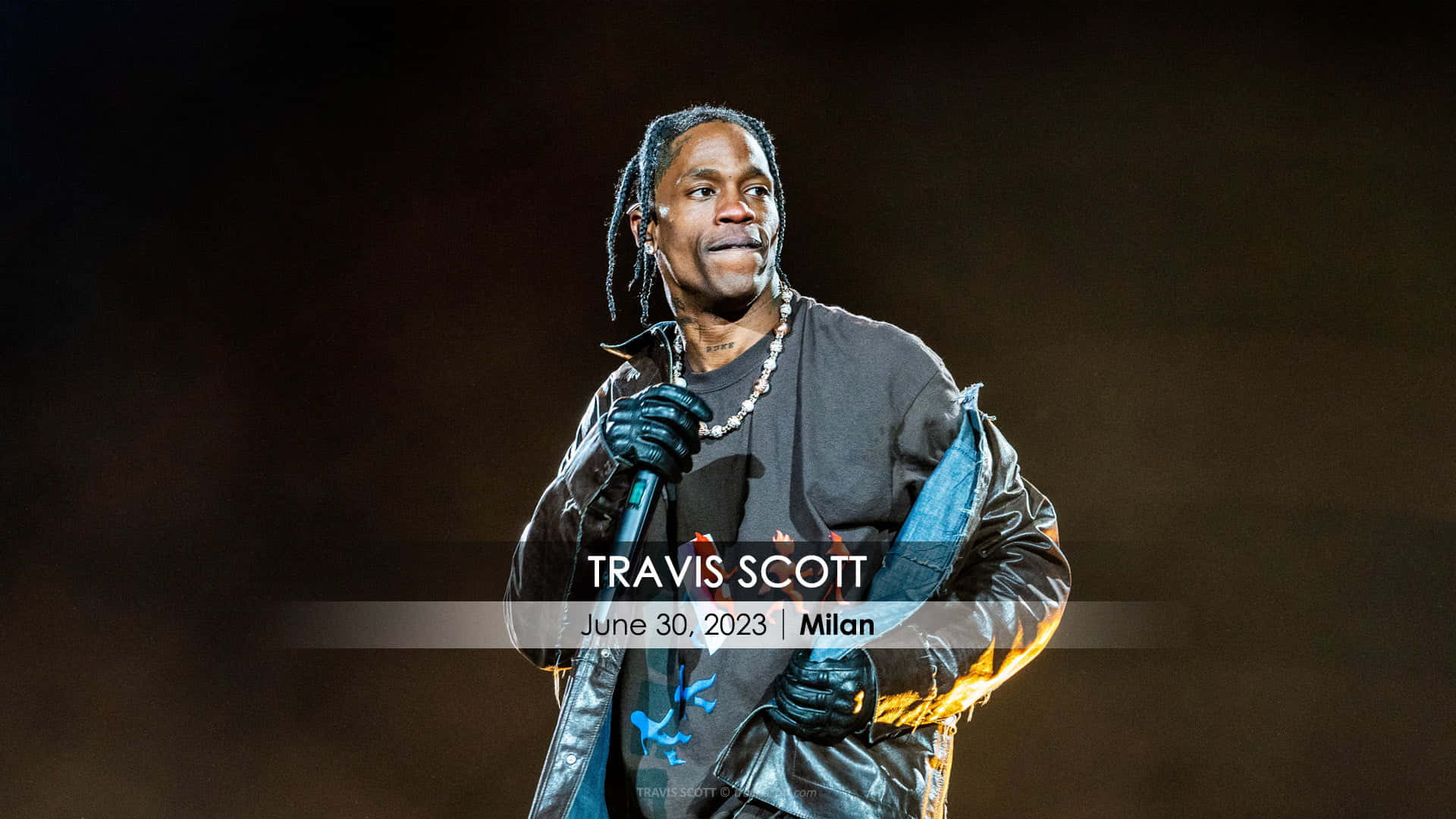 崔維斯·史考特 桌布 壁紙 — Travis Scott 在米蘭舞台上表演，穿著黑色皮夾克和手套，在明亮的舞台燈光下。