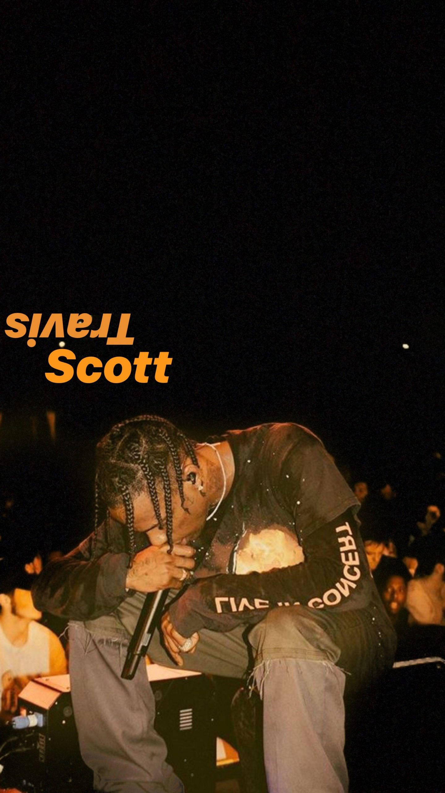 崔維斯·史考特 桌布 壁紙 — Travis Scott 在黑暗舞台上靠近麥克風，背後有發光橙色文字。