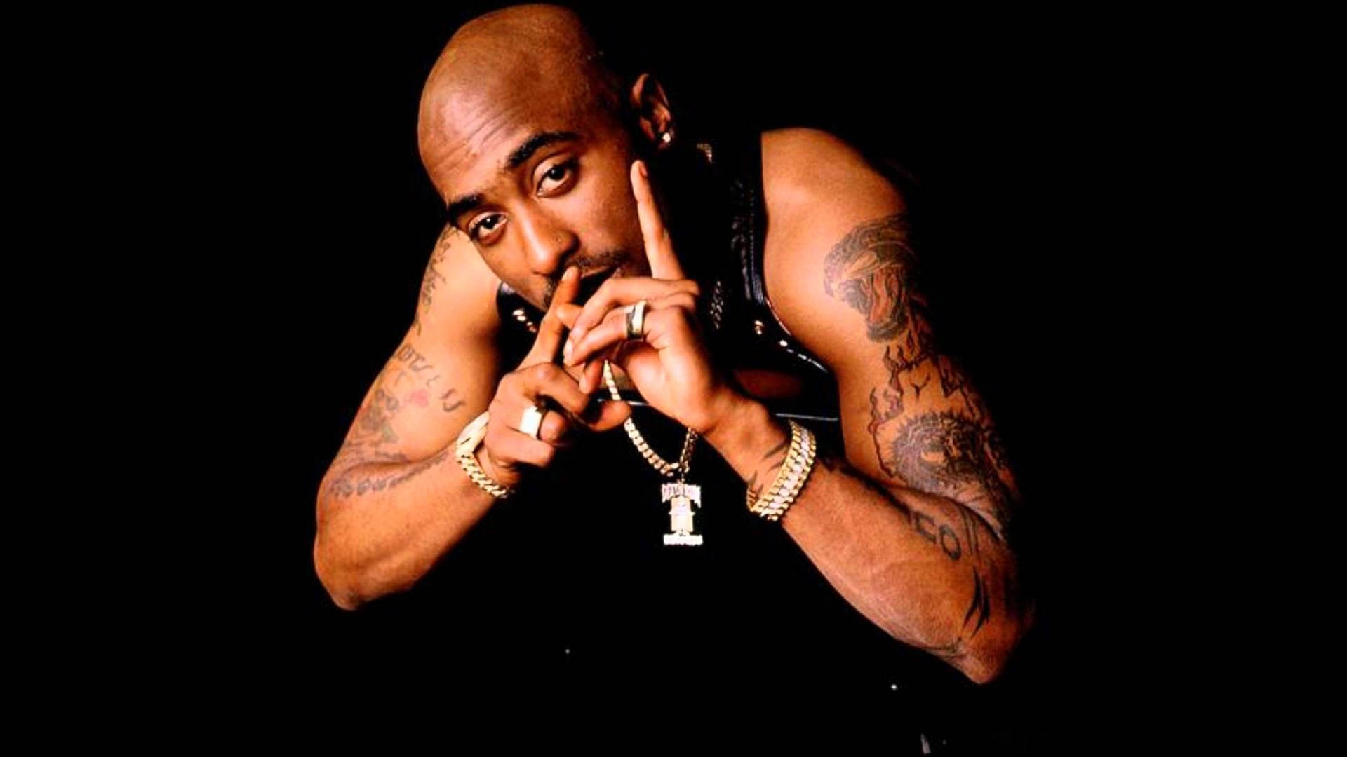桌布 壁紙 — Tupac Shakur 在黑色背景前強烈擺姿勢，帶有刺青和金飾。