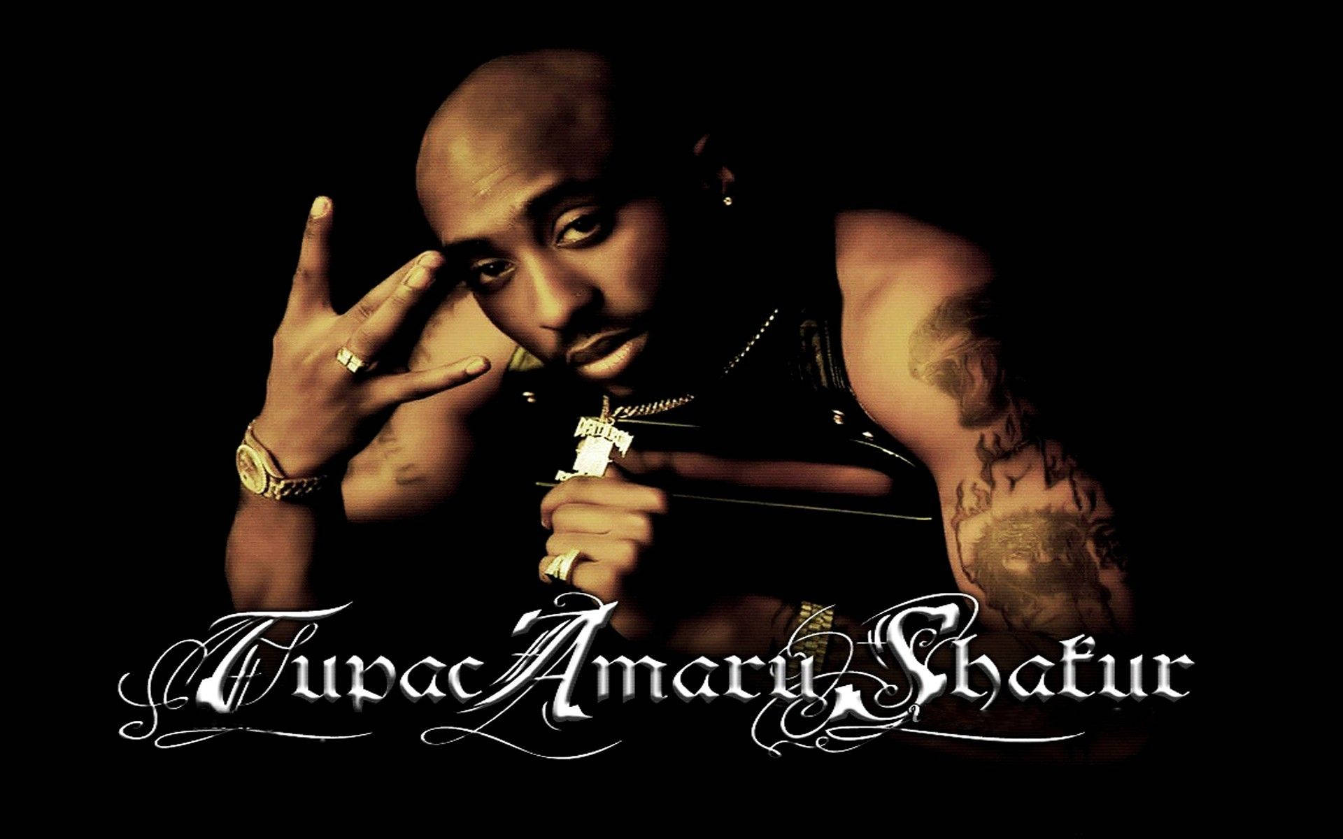 桌布 壁紙 — Tupac Shakur 在黑色背景前強烈擺姿勢，身上有刺青和珠寶，下方有華麗的白色字體寫著他的名字。