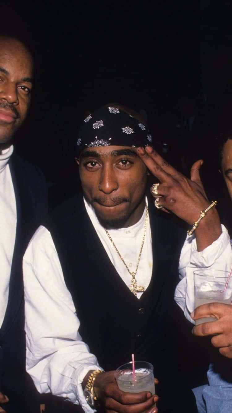  壁紙 — Tupac Shakur 戴著黑色頭巾和金鏈，在燈光昏暗的派對上擺出和平手勢。