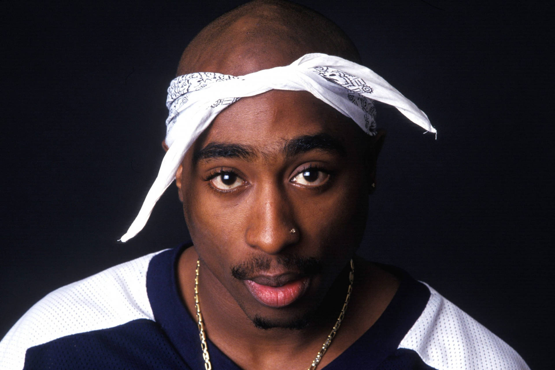 Tupac Shakur 在攝影棚肖像中戴著白色頭巾和金鏈。