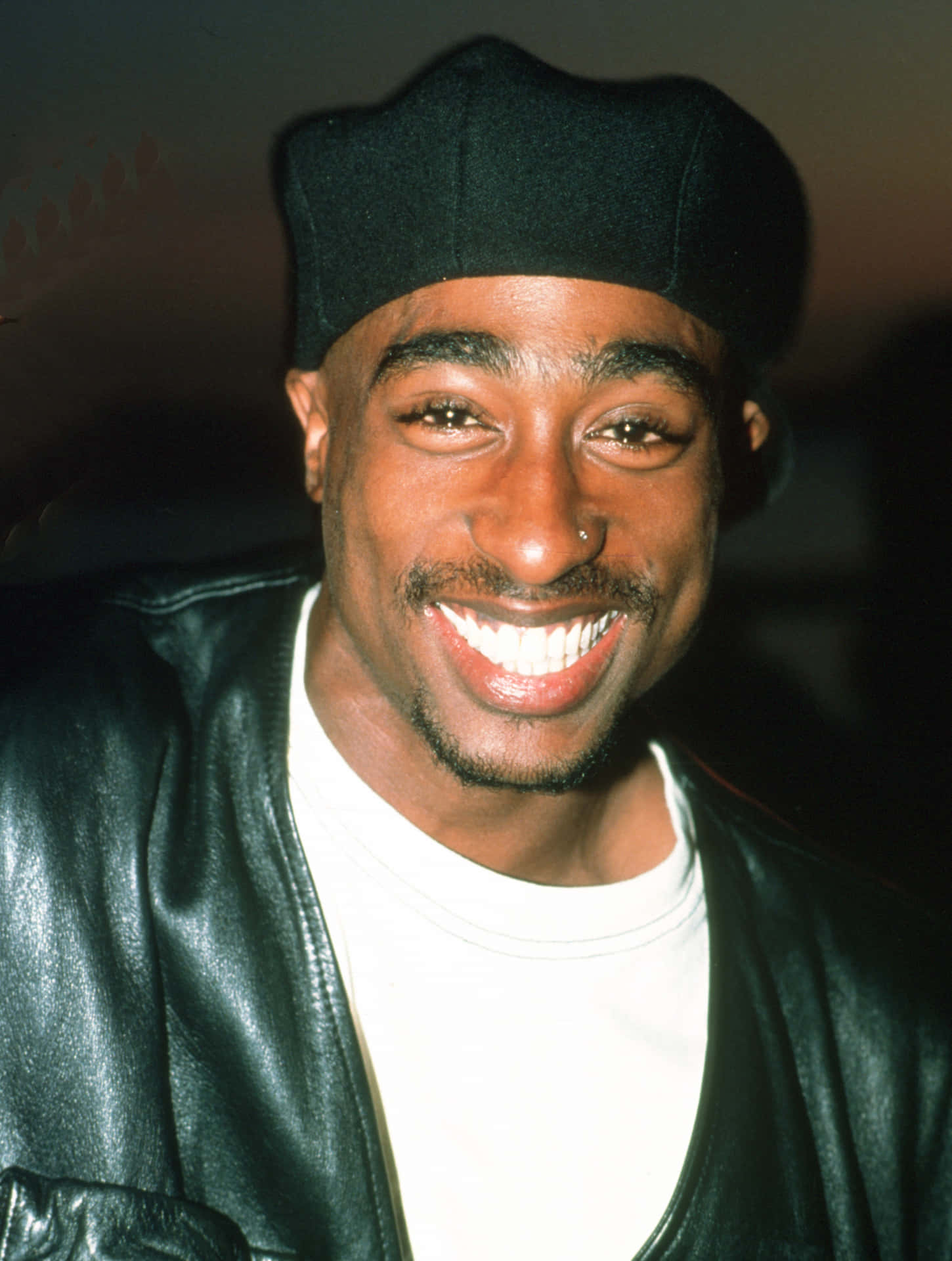 tupac 桌布 壁紙 — Tupac Shakur 的近距離肖像，他戴著黑色毛帽和皮夾克，燦爛地微笑。