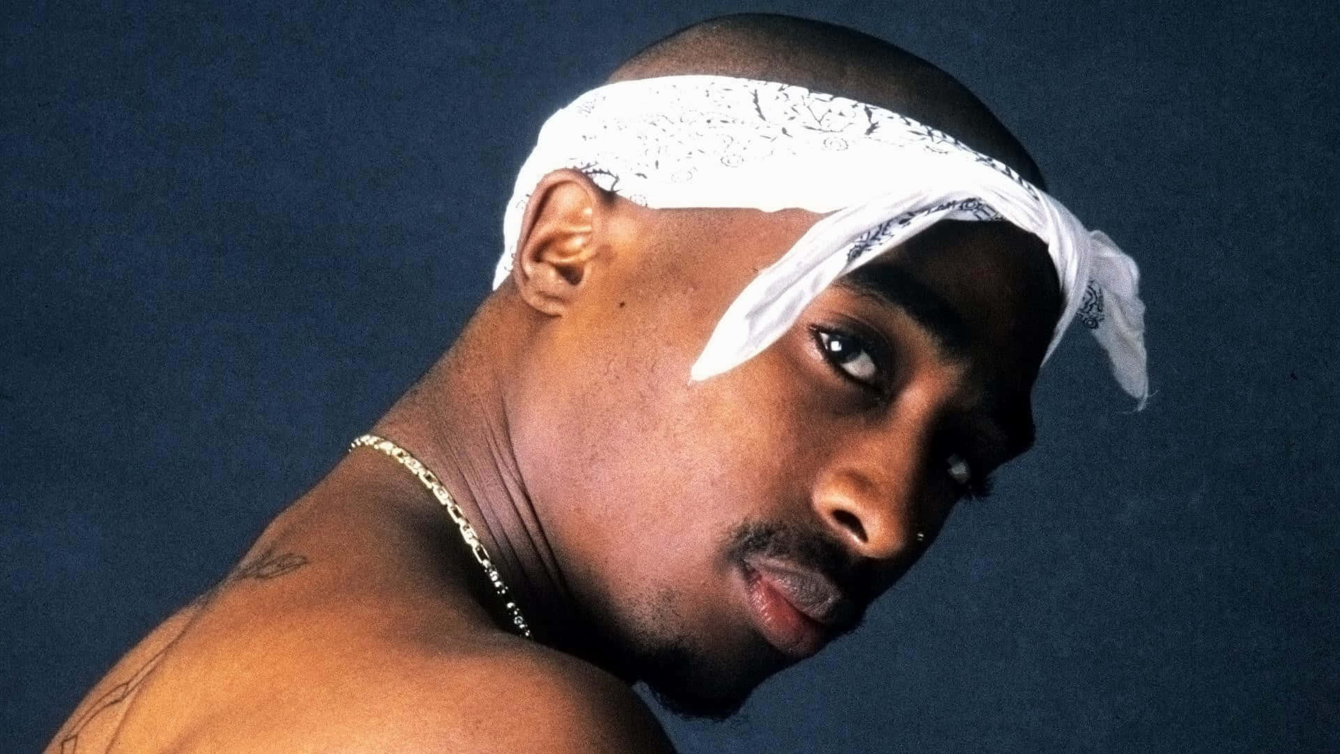 tupac 桌布 壁紙 — Tupac Shakur 的近距離肖像，戴著白色頭巾和金鏈，背景是深藍色。