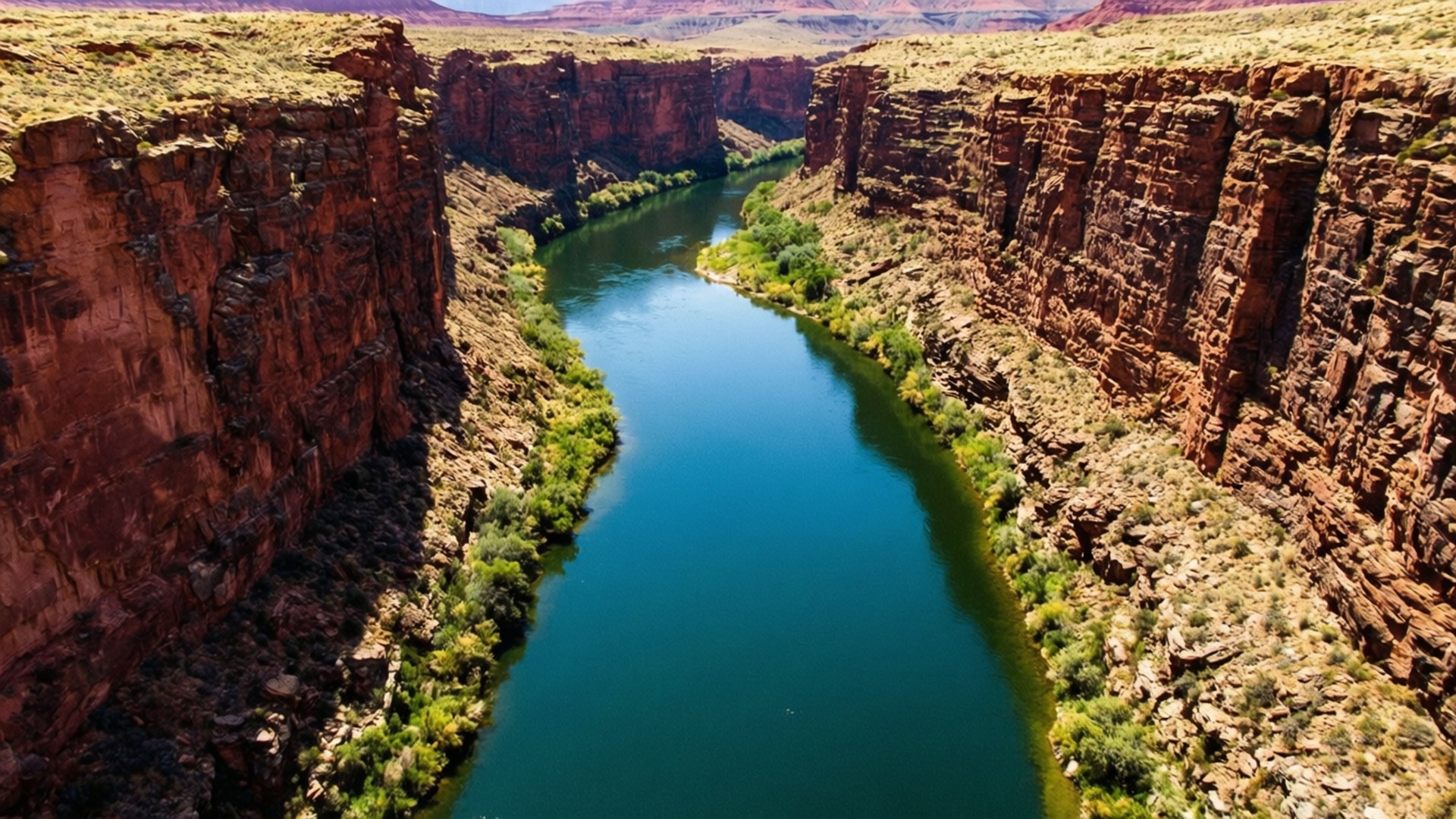 Pecos River Canyon 壁紙 — 一條蜿蜒的碧綠河流在明亮的陽光下穿過高聳的紅色岩石峽谷壁。