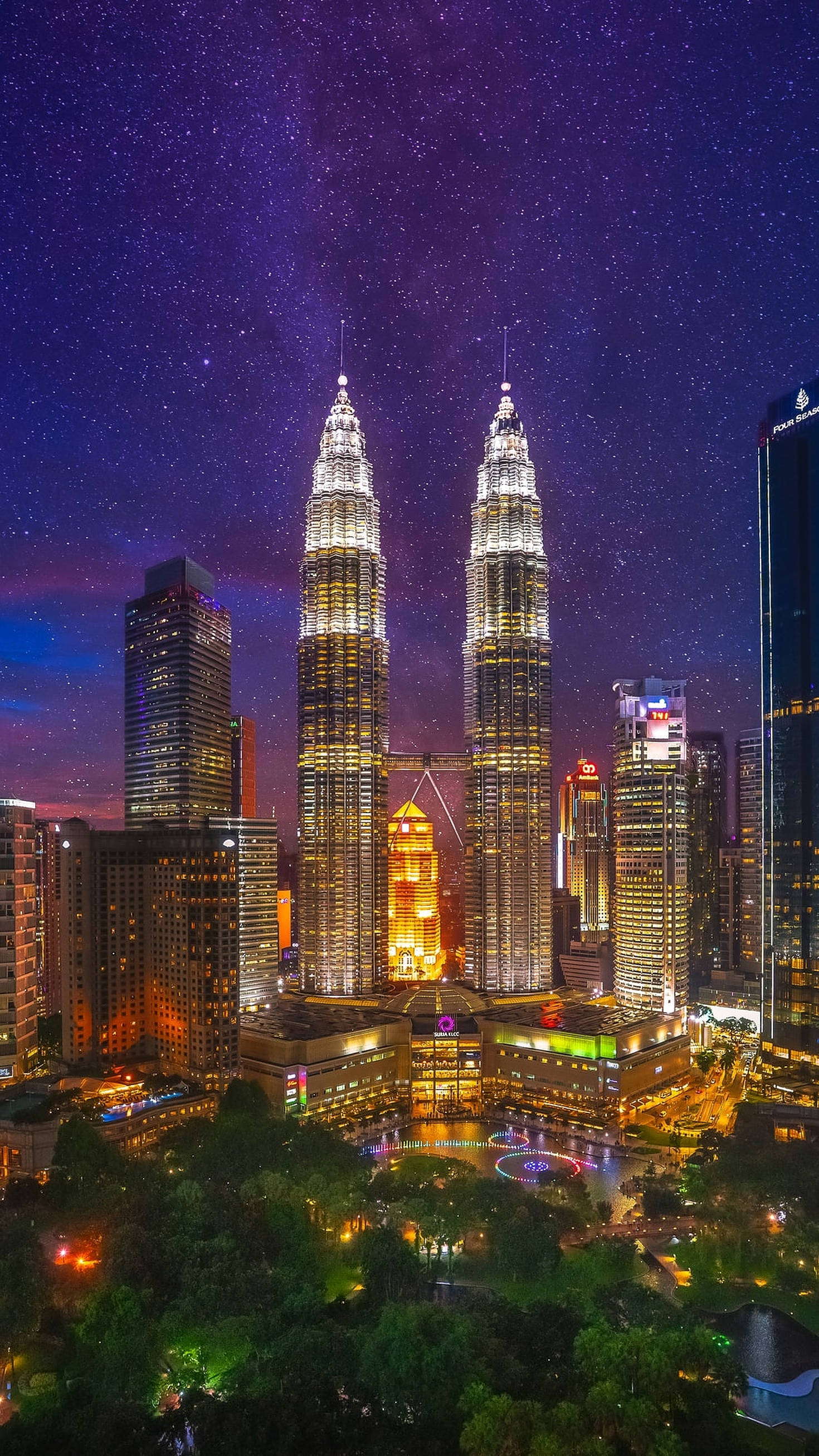 Kuala 桌布 壁紙 — Twin skyscrapers glow under a starry night sky above a vibrant cityscape with glowing lights and lush greenery below.