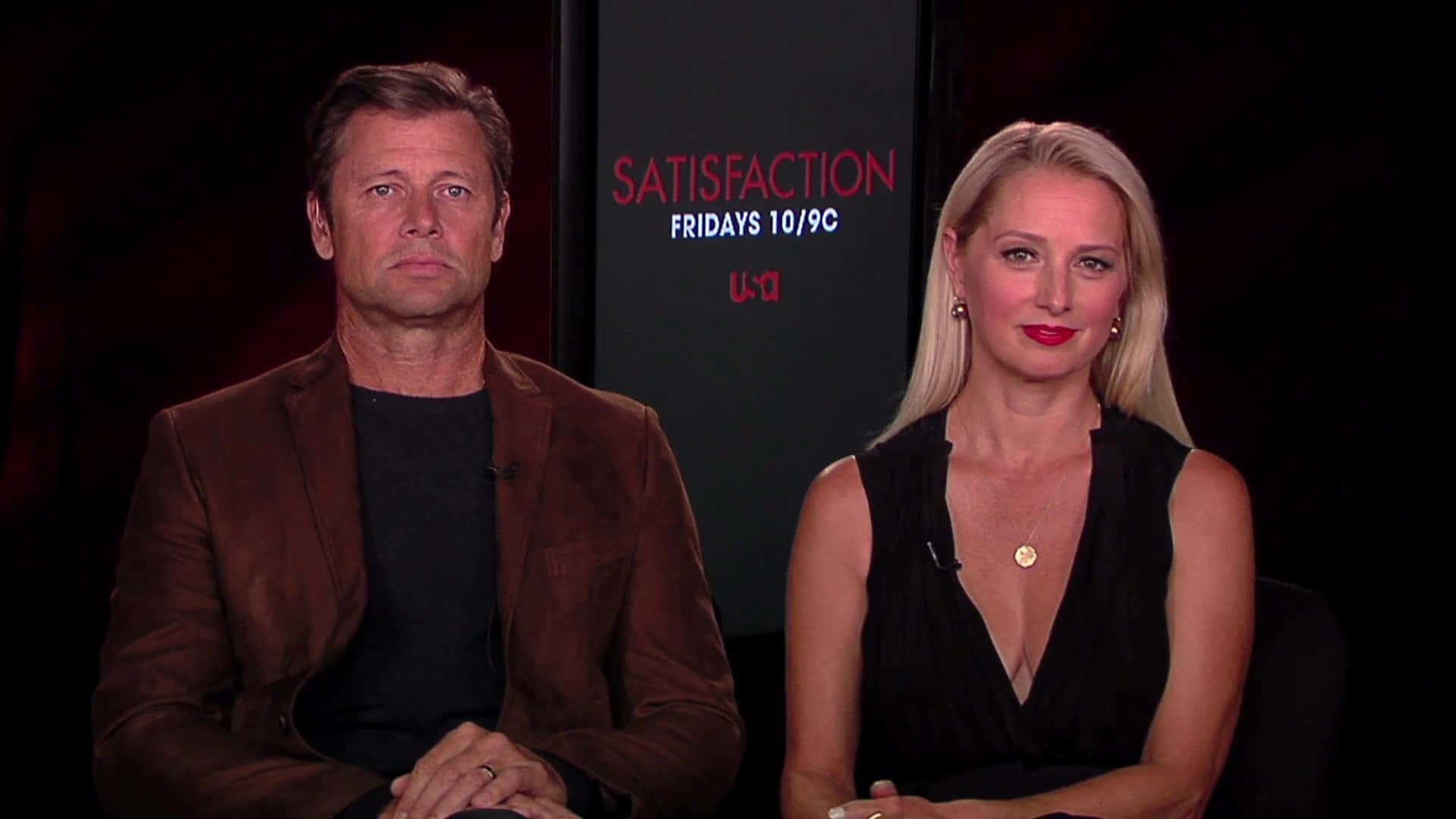 Katherine Lanasa 桌布 壁紙 — 兩位演員平靜地坐在顯示節目名稱「Satisfaction」和播出時間的黑暗背景前。
