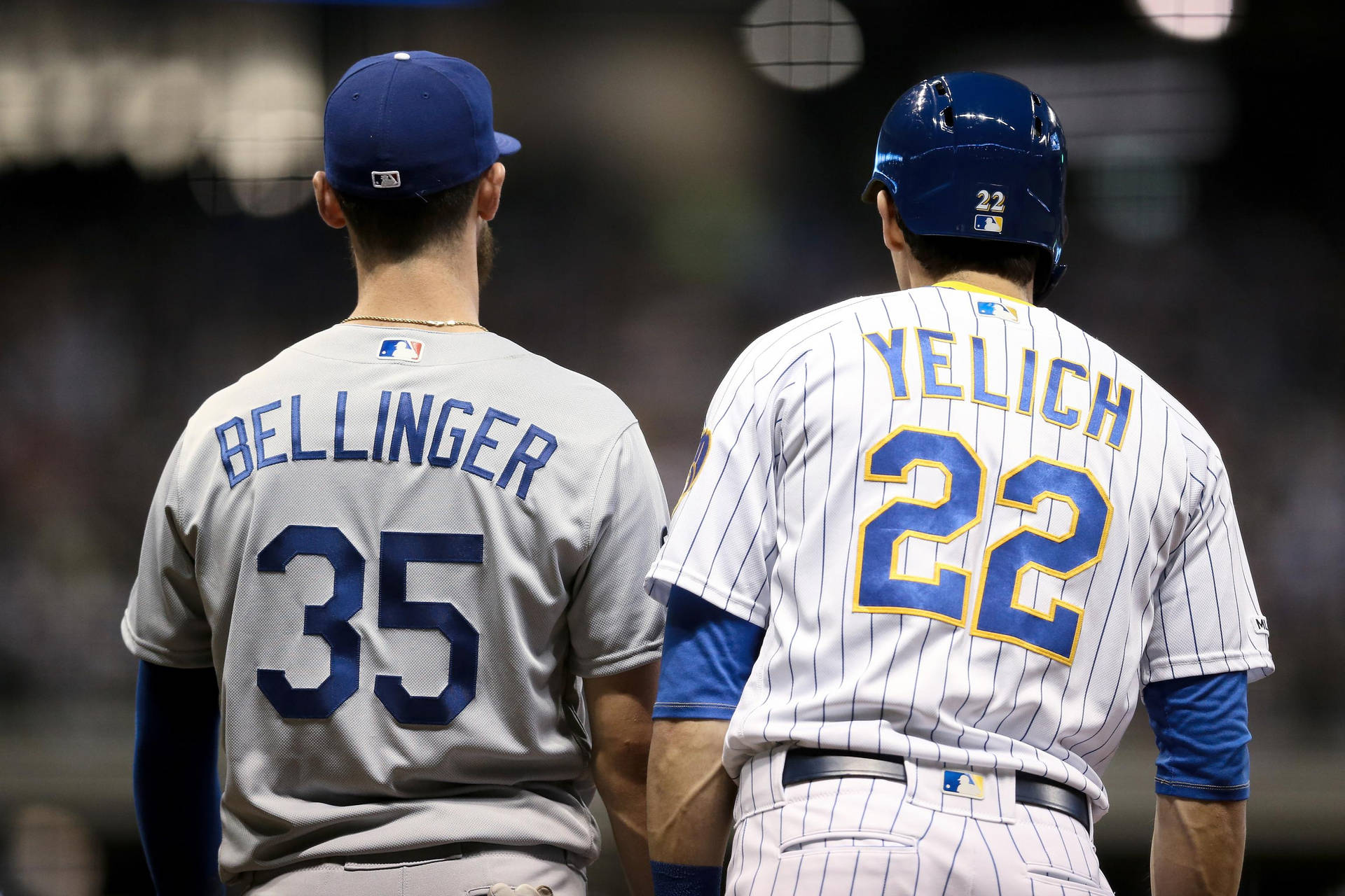 兩名身穿制服的棒球運動員在夜晚的球場上背對背站立。 — MLB 壁紙