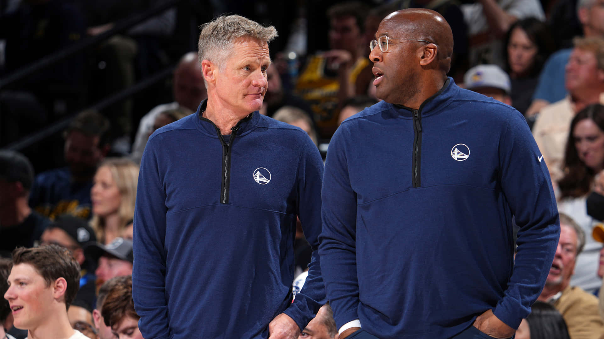 兩位身穿藍色球隊套頭衫的籃球教練在比賽期間交談。 — NBA 壁紙