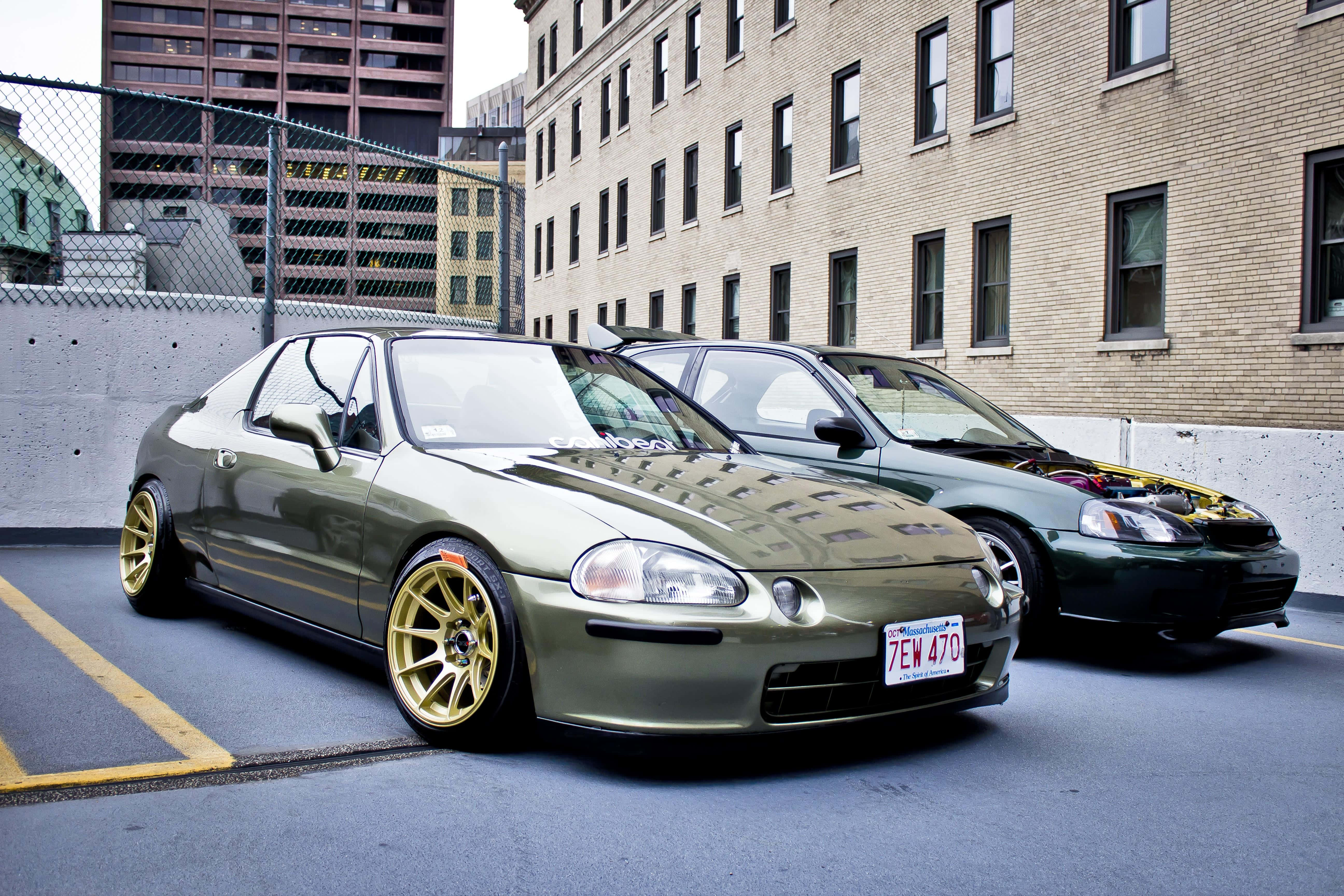 Honda Civic Del Sol 桌布 壁紙 — 兩輛定製的本田轎跑車停在城市地塊上，一輛橄欖綠配金色輪圈，另一輛深綠色配外露引擎。