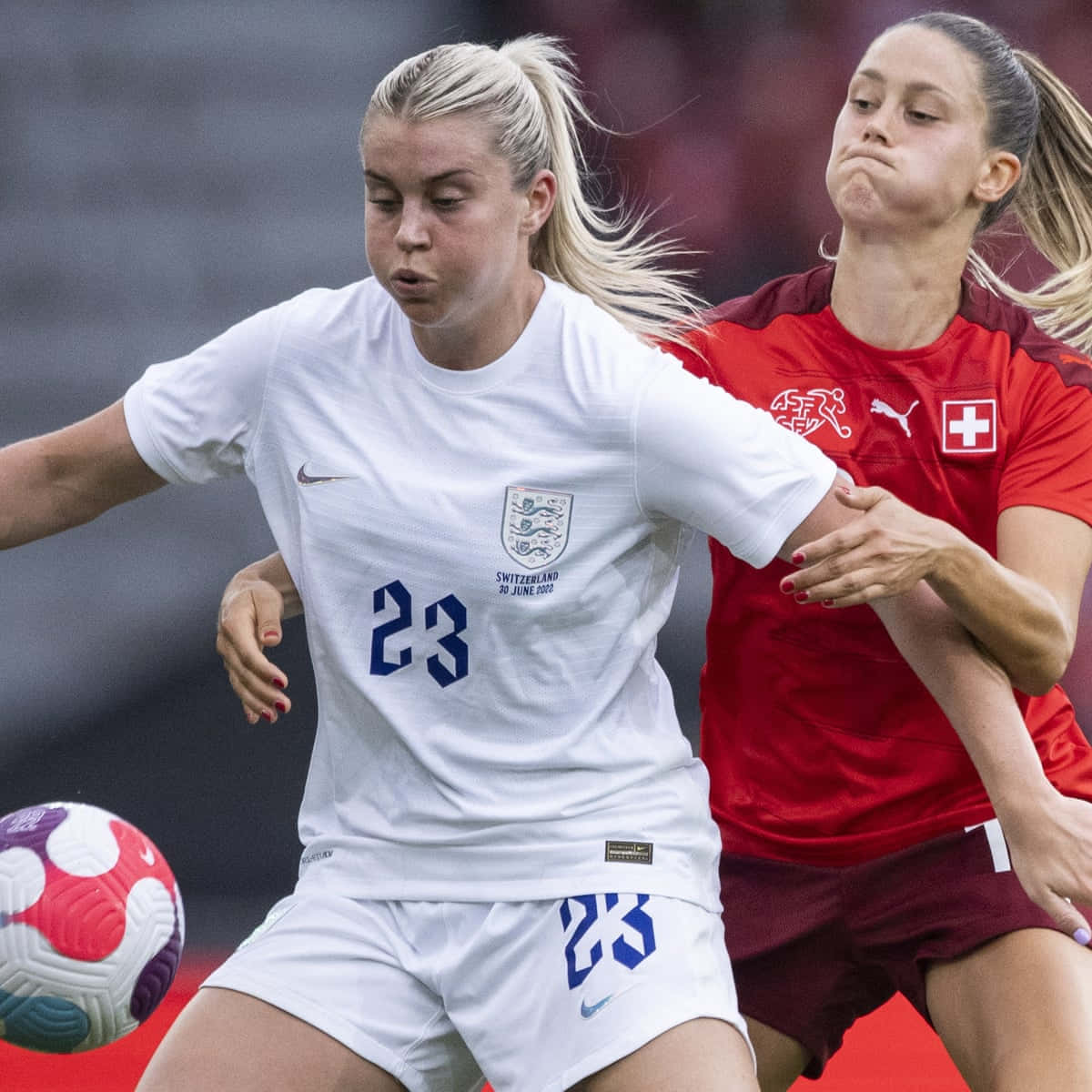 Girls Soccer 桌布 壁紙 — 兩名女足球員在比賽中激烈爭球，一人身穿白色英格蘭球衣，另一人身穿紅色瑞士球衣。