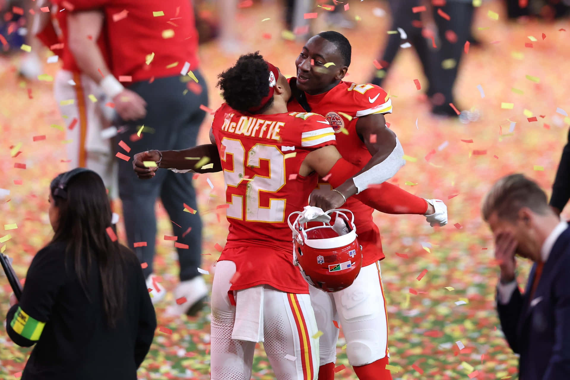  壁紙 — 兩名身穿紅色球衣的足球員在勝利後歡喜地擁抱，彩紙如雨般灑落在球場上。