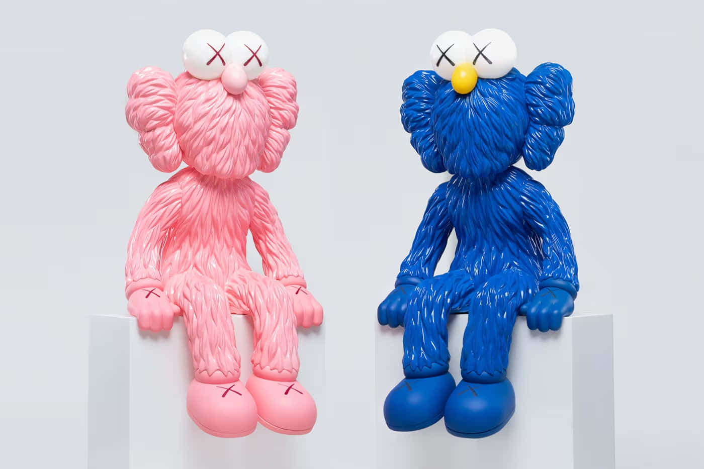  壁紙 — 兩件光面粉紅色和藍色KAWS Companion雕塑並排坐在白色底座上，背景簡潔。