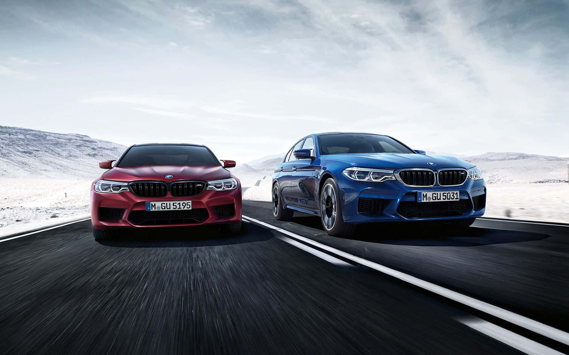 Bmw M5 桌布 壁紙 — 兩輛高性能紅色和藍色BMW M5轎車在多雲的天空下，在積雪的山路上並排競速。