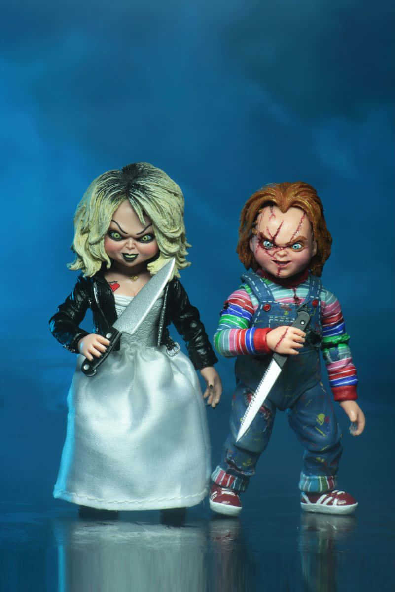 壁紙 — 兩個恐怖娃娃角色：Chucky 和他的新娘，在深藍色工作室背景前，手持刀具，地面有反射效果。