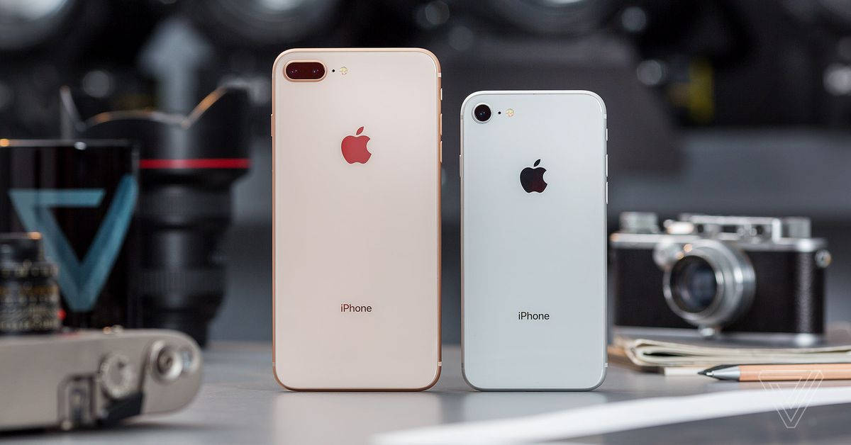 兩部金色和銀色的iPhone放在桌子上，配有復古相機和筆記本。 — iPhone 11 壁紙