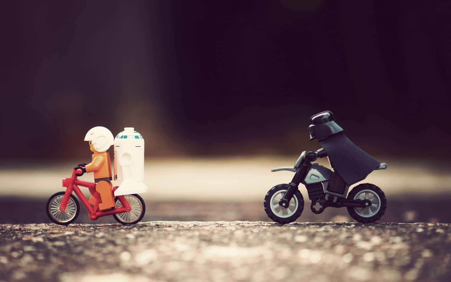  壁紙 — 兩個LEGO人偶在碎石路上騎腳踏車，一個帶著R2-D2，另一個是黑武士，充滿電影感的陰沉鏡頭。