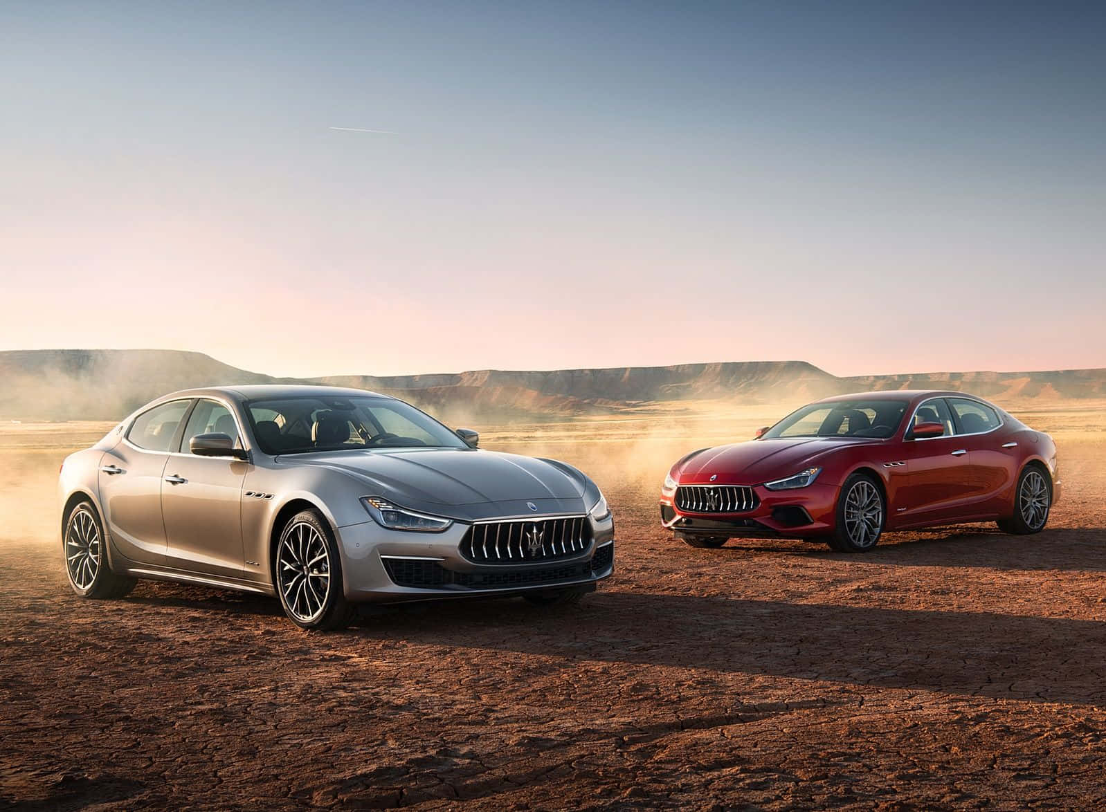 Maserati Ghibli 桌布 壁紙 — 兩輛豪華瑪莎拉蒂轎車銀色和紅色在黃昏沙漠中奔馳揚起塵土