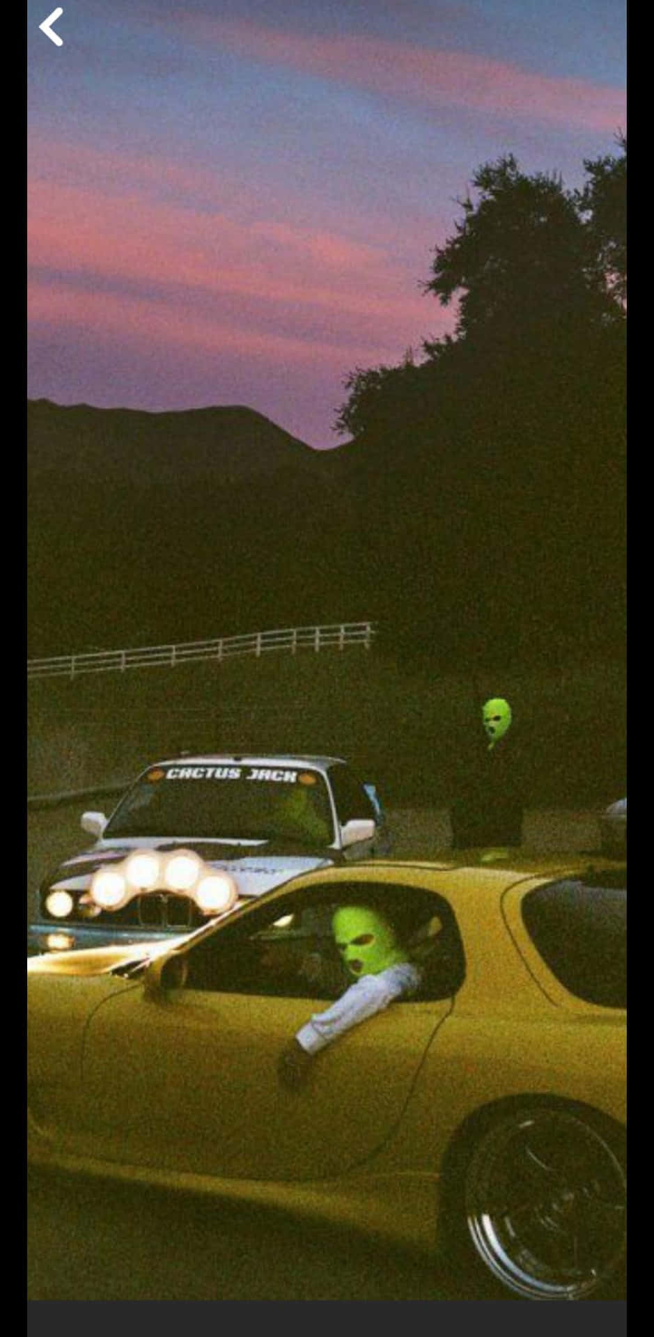  壁紙 — 兩個戴著發光綠色面罩的人物坐在定制汽車內，背景是帶有粉紅色和紫色雲彩的暮色天空。