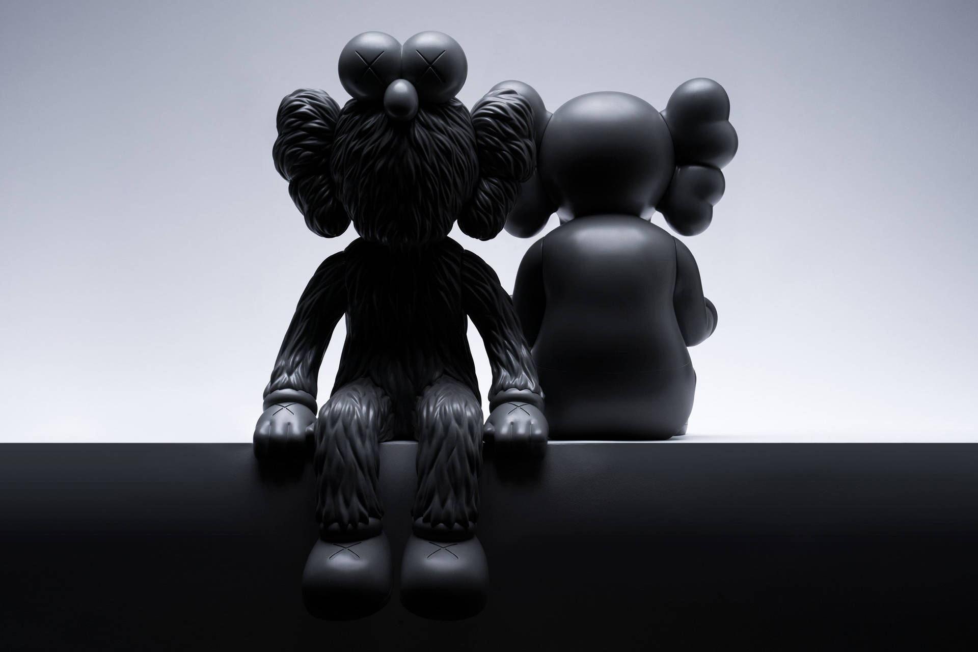 兩個黑色KAWS公仔背對背坐在黑色表面上。 — Kaws 壁紙