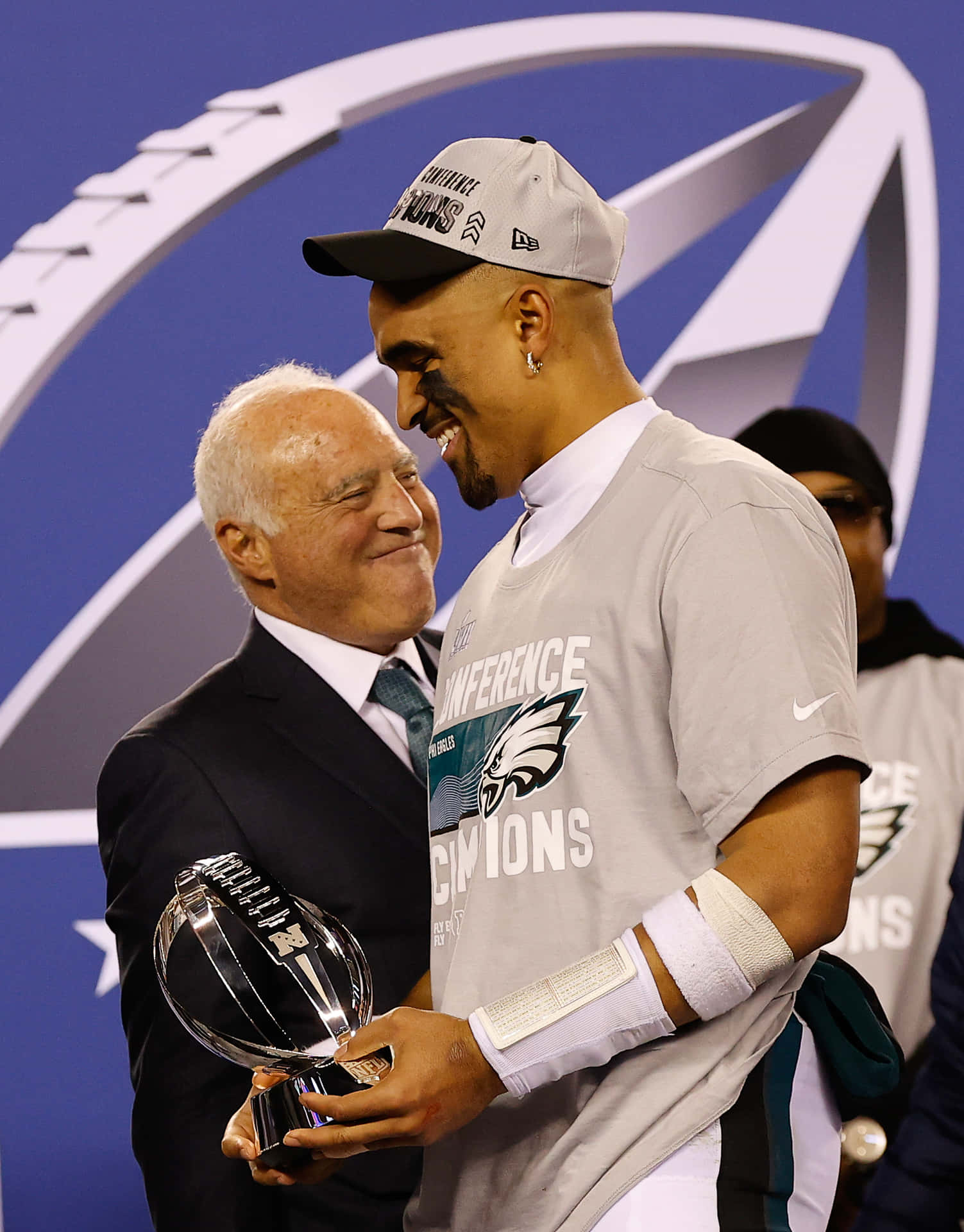  壁紙 — 兩個男人分享歡樂時刻，一位穿著「Conference Champions」球衣的足球員與一位穿西裝的長者一起舉起獎盃。