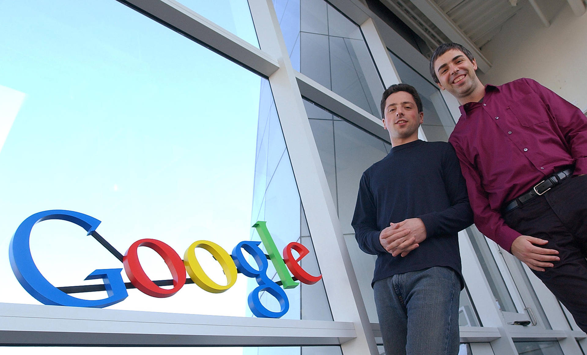 兩名男子在玻璃建築的Google標誌旁擺姿勢。 — Google 壁紙