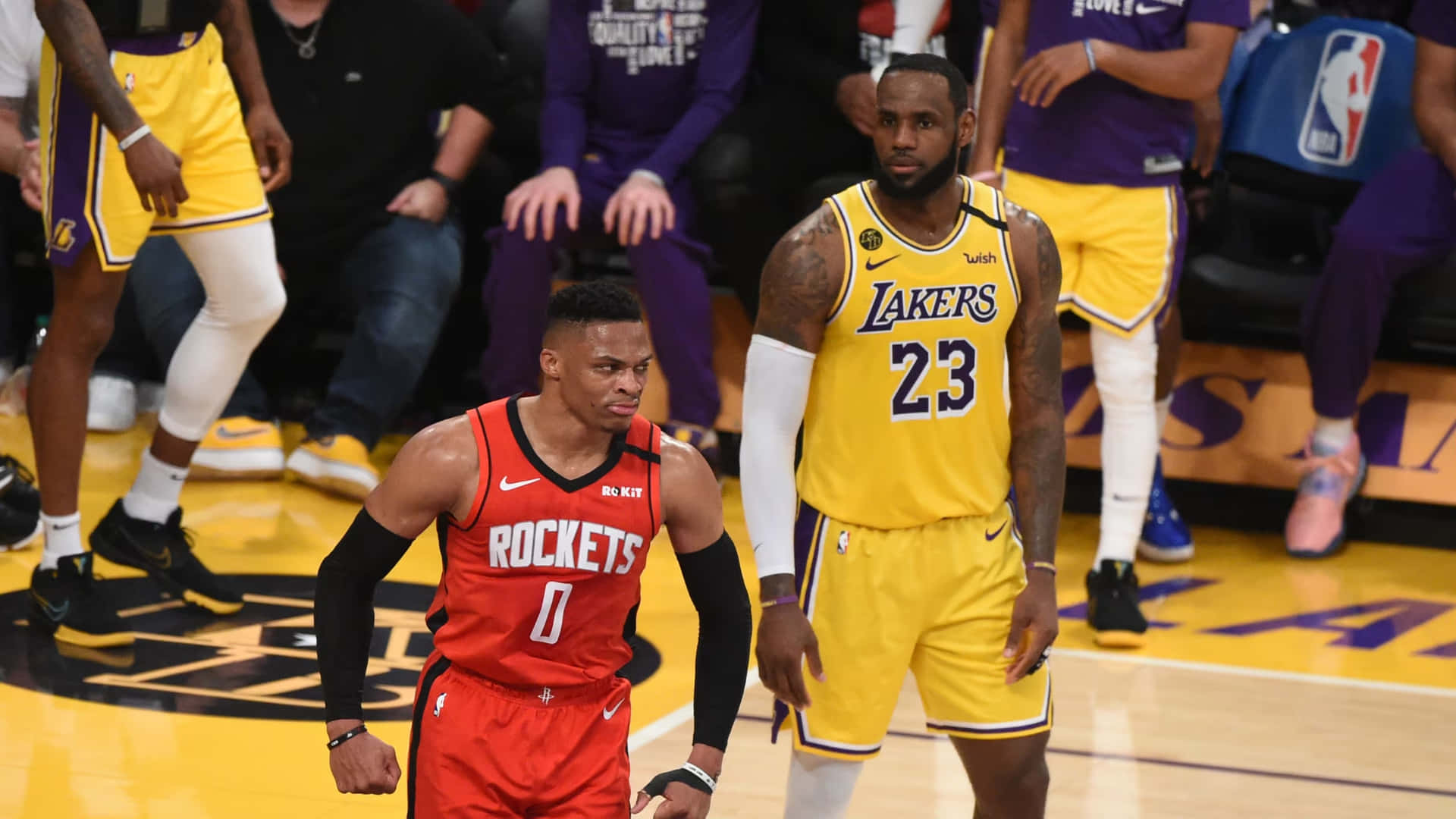  壁紙 — 兩名身穿紅黃球衣的NBA球員在籃球場上比賽，背景有隊友和觀眾。