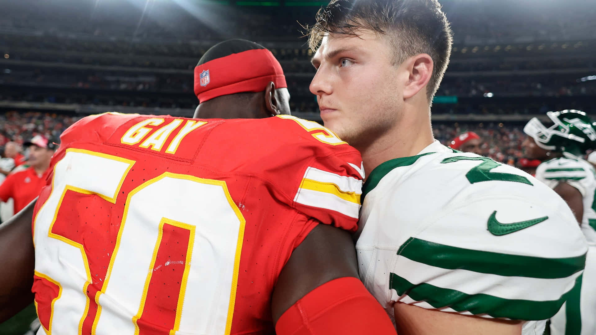  壁紙 — 兩名身穿紅白球衣的NFL球員在比賽期間於燈光明亮的體育場上擁抱。