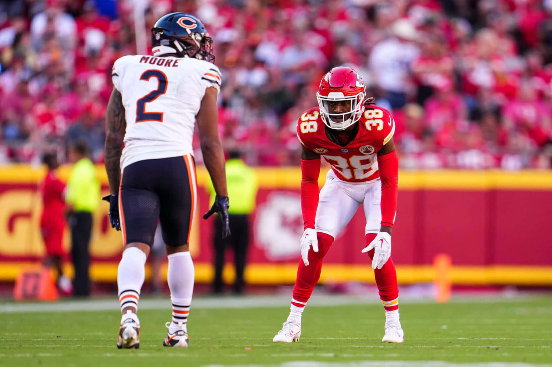  壁紙 — 兩名身穿紅白球衣的NFL球員在陽光明媚的綠色球場上對峙，身後是模糊的體育場人群。