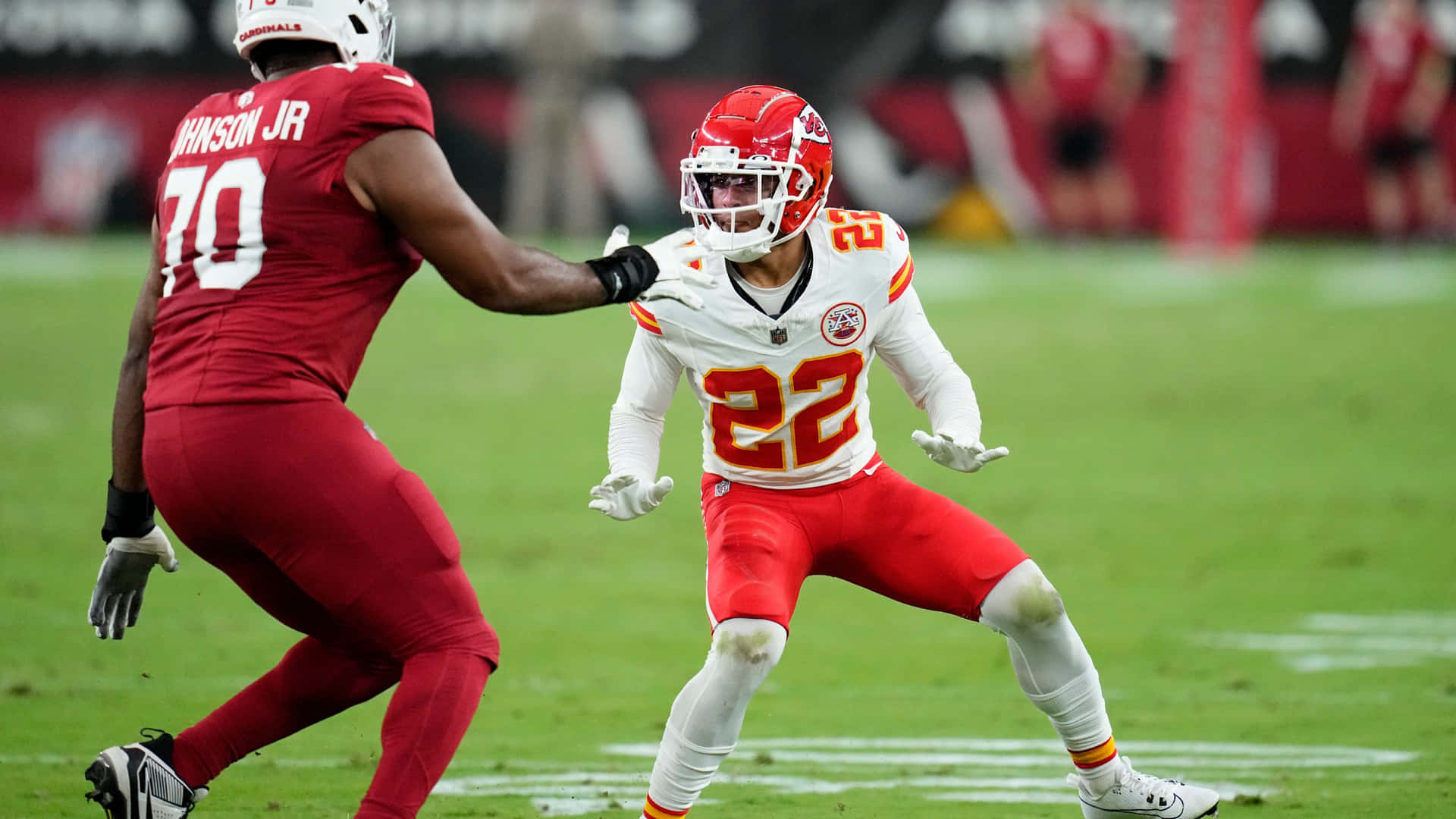  壁紙 — 兩名身穿紅白球衣的NFL球員在體育場燈光下，於充滿活力的綠色足球場上激烈競爭。
