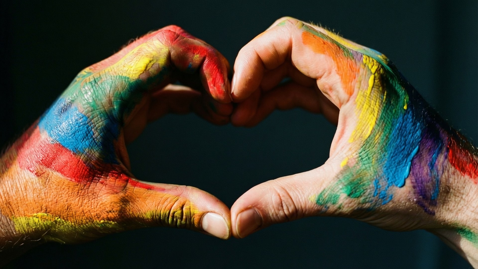 Rainbow Heart Hands 壁紙 — 兩隻沾滿油漆的手在深色背景上形成一個心形，帶有鮮豔的彩虹色。