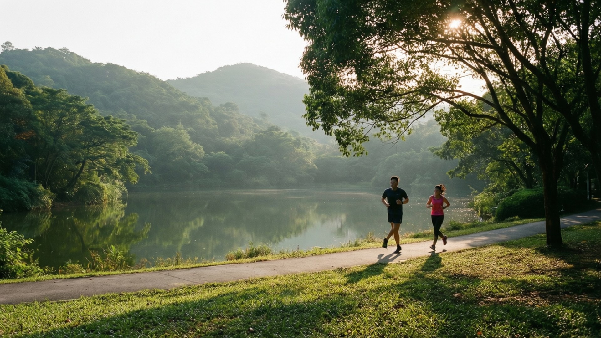 Lianhuashan Park Morning 壁紙 — 兩人在陽光明媚的湖邊小徑上慢跑，薄霧籠罩的山巒和茂密的樹木襯托出寧靜的早晨景色。