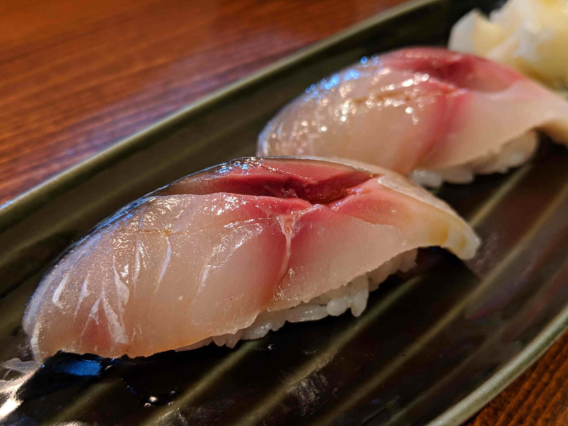  壁紙 — 兩件新鮮鮪魚握壽司在深綠色盤子上閃閃發光，旁邊有芥末。