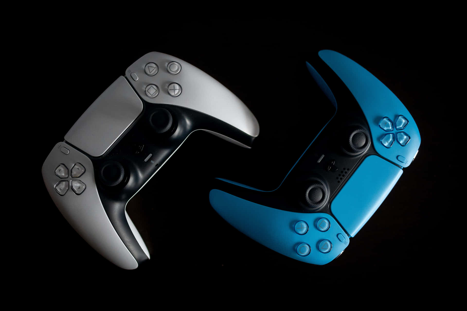 兩個 PlayStation 5 控制器，一個銀色一個藍色，在黑色背景上 — Ps4 壁紙