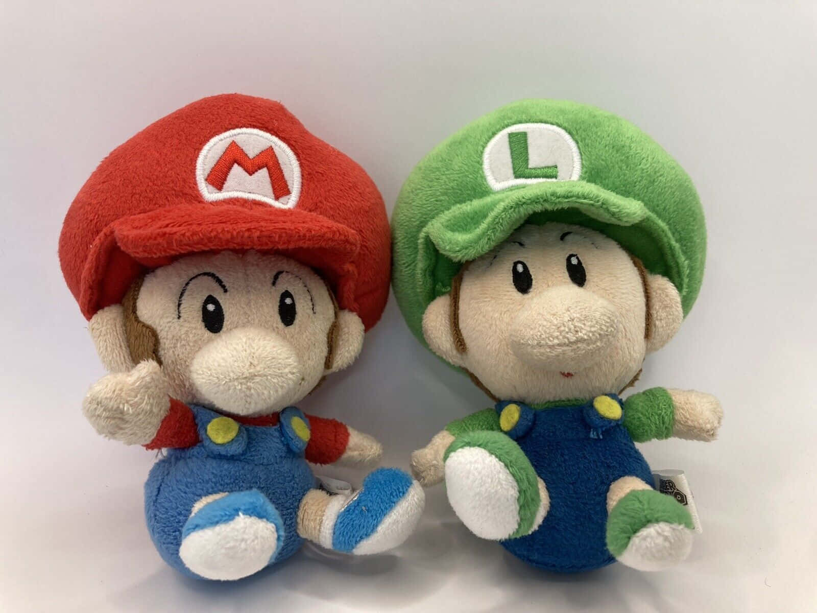 Baby Luigi 桌布 壁紙 — 兩個瑪利歐和路易吉毛絨公仔並排坐在純白色背景前。