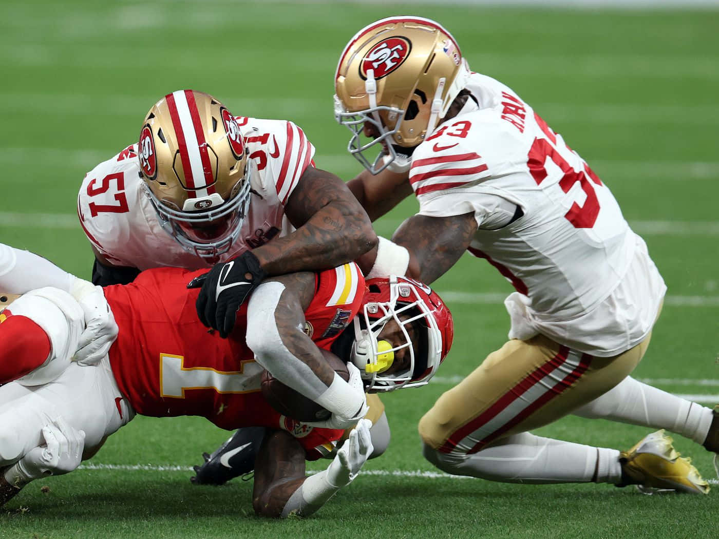  壁紙 — 舊金山四九人隊的兩名防守球員在激烈的NFL美式足球比賽中，於充滿活力的綠色球場上擒抱堪薩斯城酋長隊的一名球員。