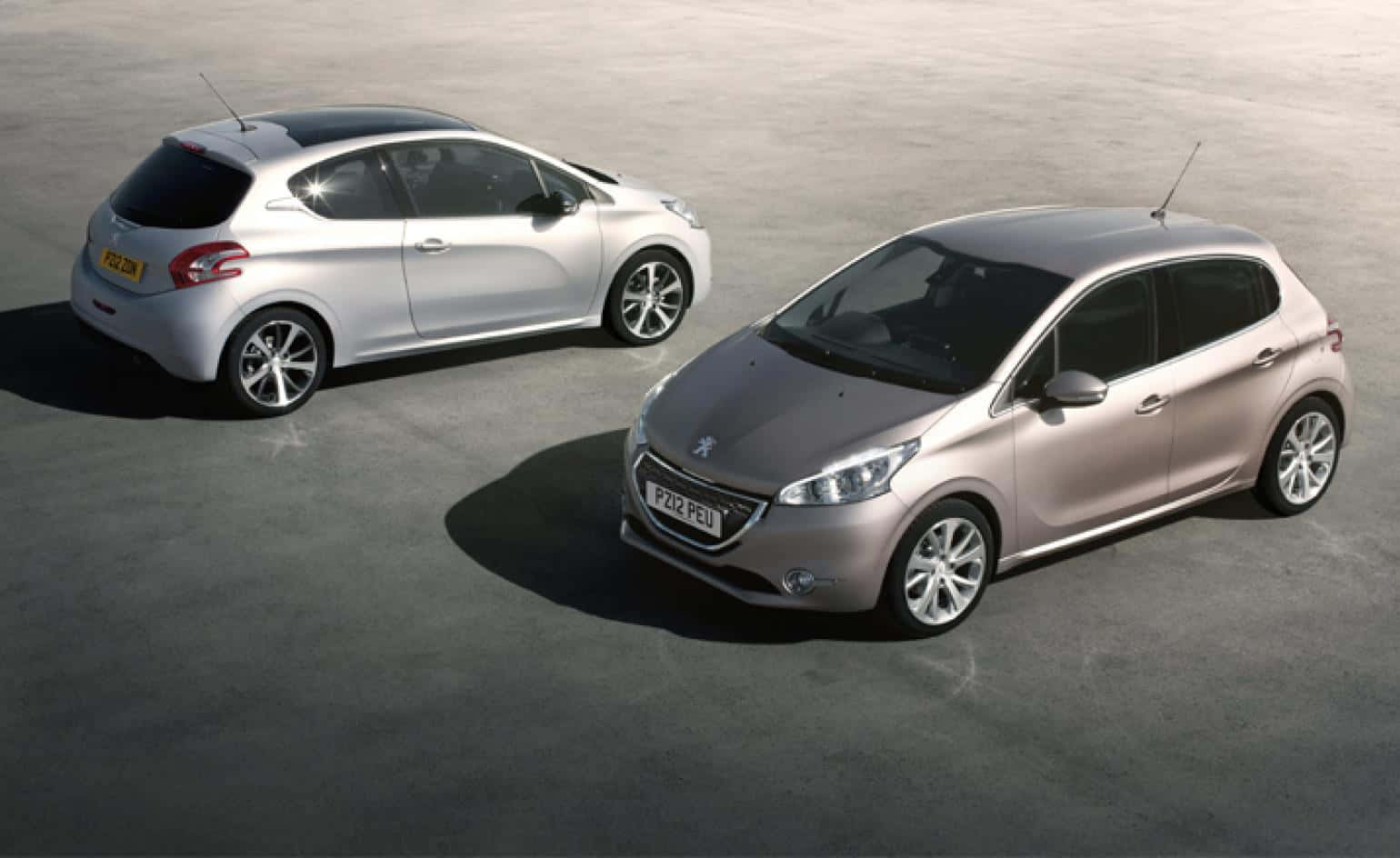 Peugeot 208 桌布 壁紙 — 兩輛時尚的Peugeot 208掀背車，銀色和玫瑰金色，停在簡約的混凝土表面上，在明亮的日光下。