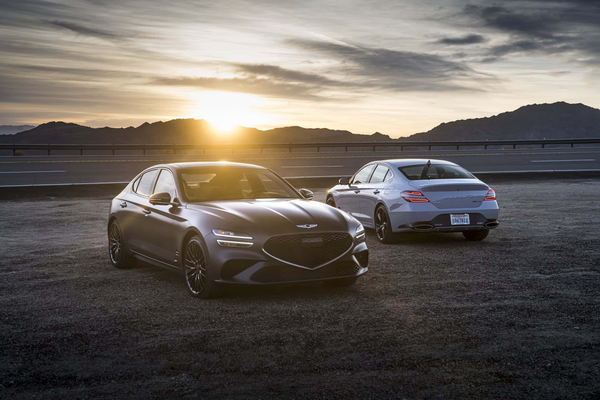 Genesis G70 桌布 壁紙 — 兩輛時尚轎車停泊在沙漠公路，背景是日落和山脈。