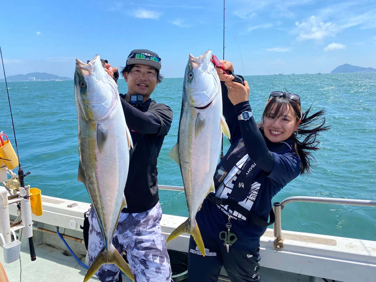  壁紙 — 兩位微笑的釣魚人自豪地展示他們在晴朗天空下、站在明亮藍色海洋上的船上捕獲的大銀魚。