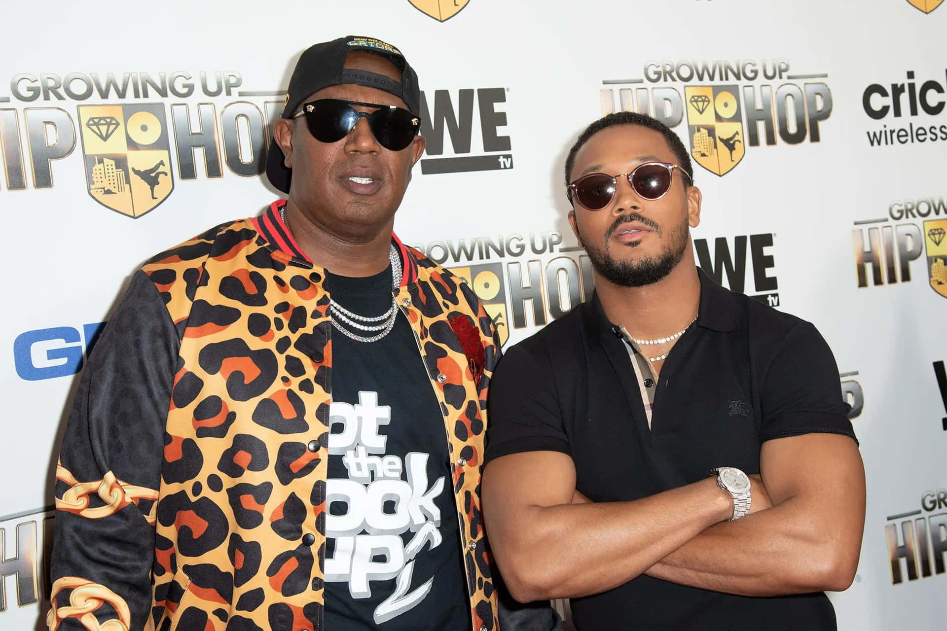  壁紙 — 兩位時尚男士戴著太陽眼鏡，在帶有品牌背景的「Growing Up Hip Hop」活動中自信地擺姿勢。