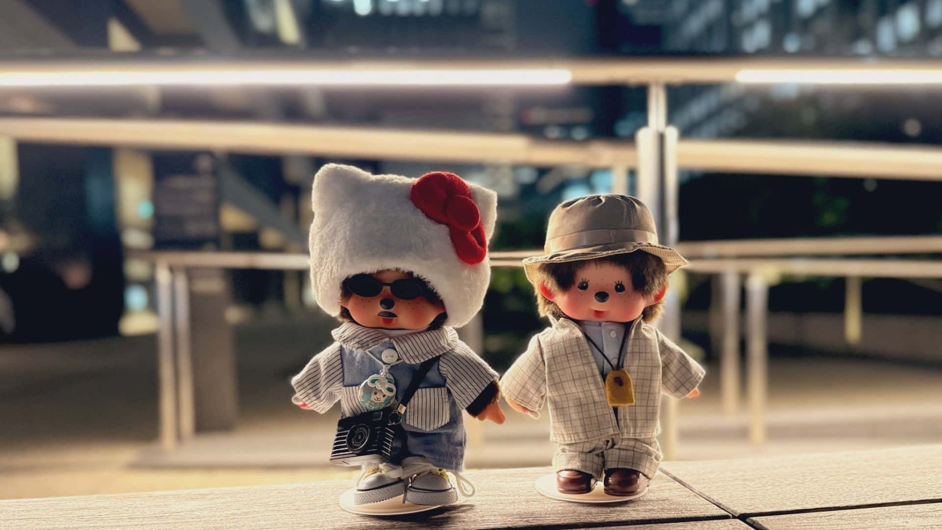  壁紙 — 兩隻時尚的蒙奇奇公仔穿著潮流服裝，在夜晚並排站在欄杆上，背後的城市燈光柔和地閃爍。