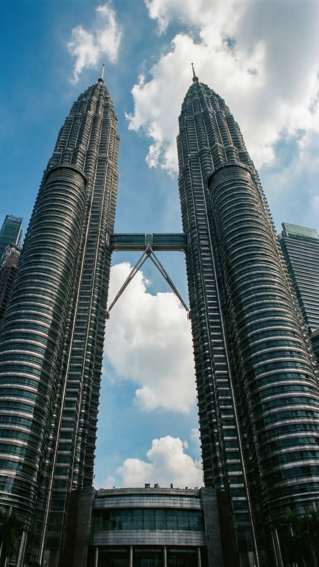 Towers Ascending 壁紙 — 兩座高聳的玻璃摩天大樓在明亮的藍天白雲下拔地而起，由一條空中走廊連接。