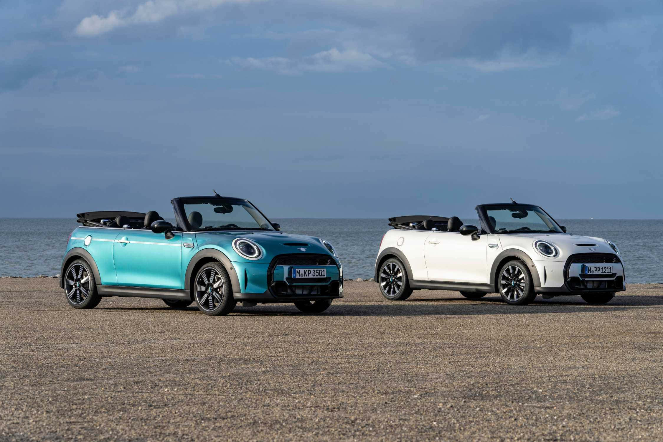 Mini Cooper S Convertible 桌布 壁紙 — 兩輛充滿活力的MINI Convertibles停泊在卵石海灘上，背景是海洋和多雲的天空。